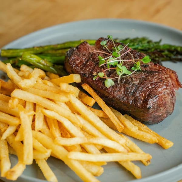 Grilled steak with microgreens, a side of golden fries, and green asparagus on a gray plate.