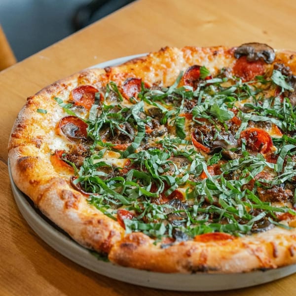A New American pizza from Ednas Market & Grille, topped with pepperoni, mushrooms, and fresh basil.