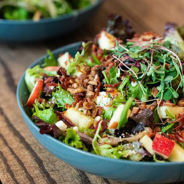 Close-up of a vibrant salad with greens, apples, bacon, and microgreens in a blue bowl.