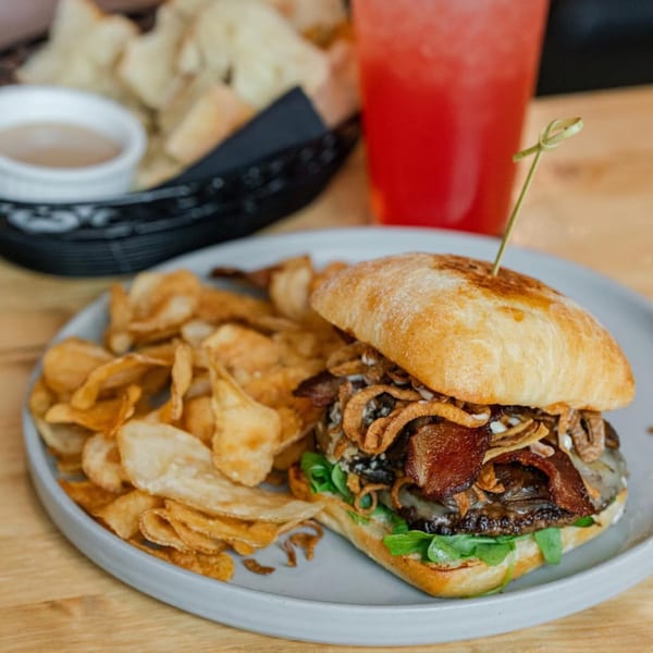 A New-American burger with bacon, crispy onions, and arugula, served with potato chips.