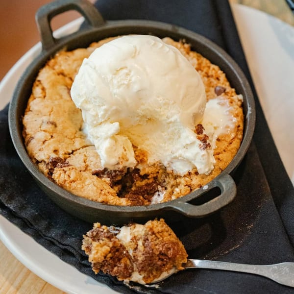 Warm chocolate chip cookie skillet with melting vanilla ice cream, a spoonful removed.