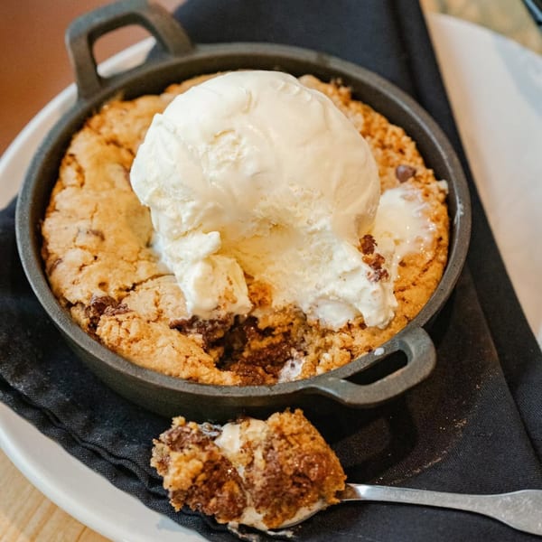 Warm chocolate chip cookie skillet with melting vanilla ice cream and a spoonful removed.
