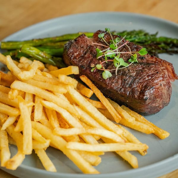 Grilled steak with microgreens, golden french fries, and green asparagus on a gray plate.