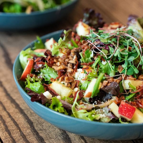 A vibrant Ednas Market & Grille salad with greens, apples, bacon, cheese, and microgreens.