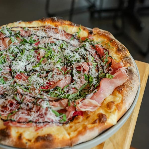 A New American pizza from Ednas Market & Grille, topped with prosciutto, basil, and balsamic glaze.