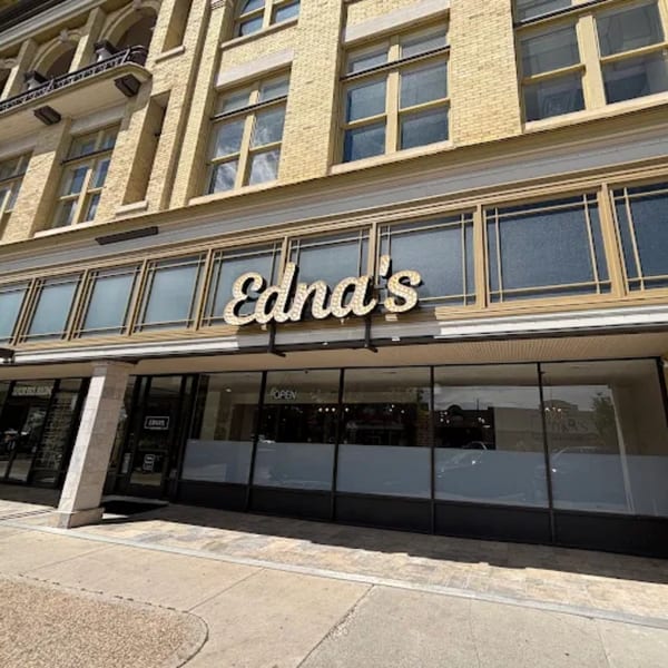 The exterior of Edna's Market & Grille, a New American restaurant, with its illuminated sign and large windows.