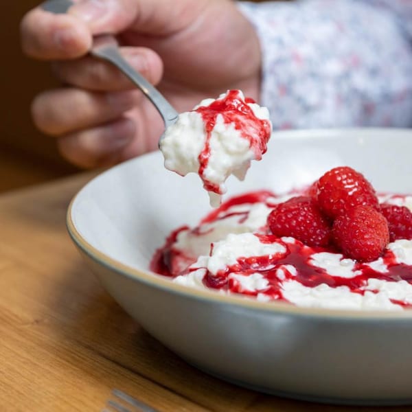 A spoon lifts creamy rice pudding with raspberry sauce and fresh raspberries from a bowl.