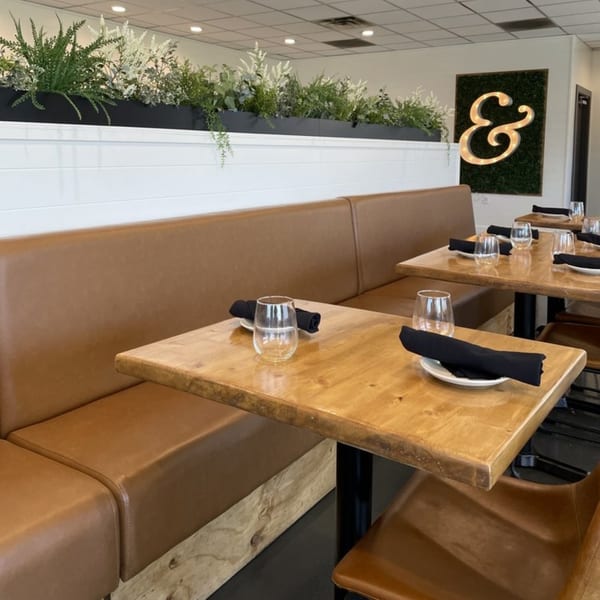 Ednas Market & Grille dining room with brown leather banquettes, wooden tables, and a lighted ampersand sign.